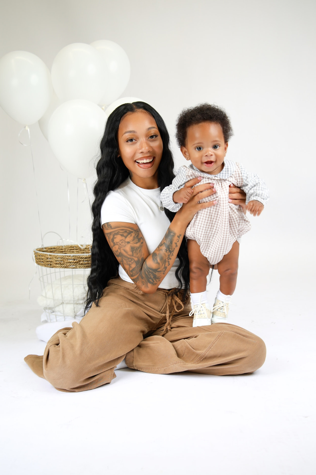 A mom smiling as she holds her baby up beside balloons